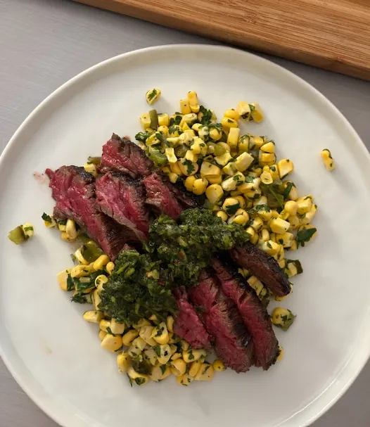Sliced chimichurri skirt steak with caramelized Japanese yams, corn salsa, chimichurri, and garlic sauce.